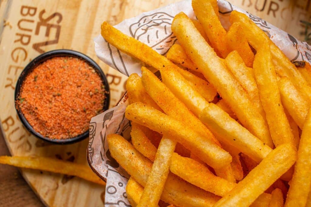 Delicious crispy french fries with a side of spicy seasoning, perfect for a snack.
